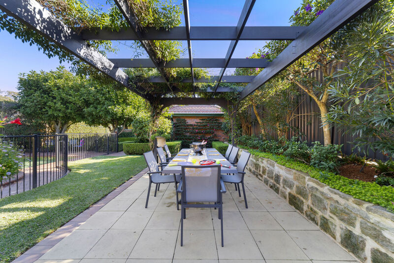 Outdoor dining table set beneath a vine-covered pergola on a sandstone terrace