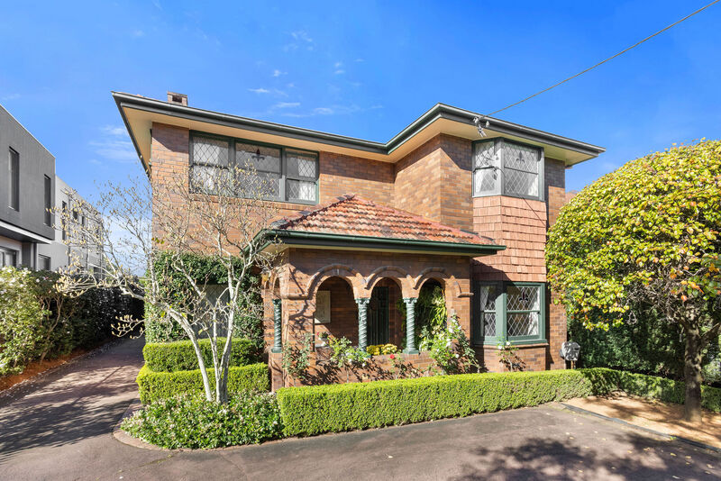 The two-storey double-brick facade of 32 Wallis Avenue with its arched portico, behind clipped hedges