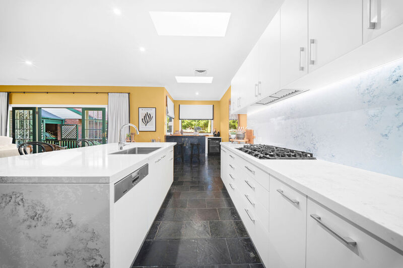 Kitchen with a white stone island, white splashback and skylights